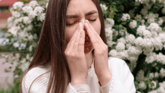 Una noia es tapa el nas i tanca els ulls davant una planta florida. Probablement té al·lèrgia primaveral