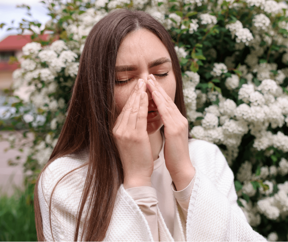 Una noia es tapa el nas i tanca els ulls davant una planta florida. Probablement té al·lèrgia primaveral