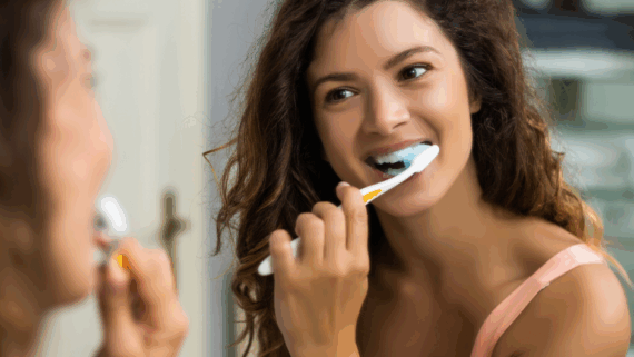 una noia es raspalla les dents davant elmirall per tenir una boca sana